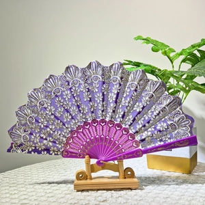 Detail of purple folding fan with golden floral patterns and lace trim on a stand