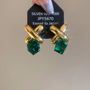 Close-up of gold X-cross earrings with dark green crystal cubes on a black display card