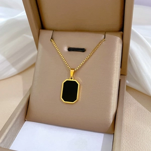 Detail of a gold square necklace with black pendant displayed in a beige jewelry box