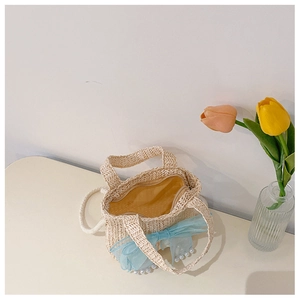Detail view of woven straw bag with blue mesh bow and decorative pearl handle