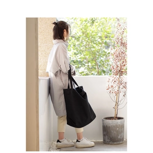 Woman wearing a large black canvas tote bag on her shoulder in a sunlit outdoor setting