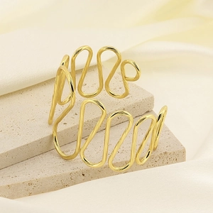Detail view of gold wave-shaped stainless steel cuff on elegant marble and satin