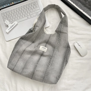 Flat lay of a grey tie-dye canvas tote bag with laptop and office accessories on white fabric
