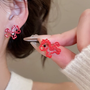 Close-up of red horse stud earrings worn on ear and held between fingers for detail