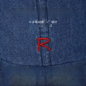Close-up of red letter R embroidery on dark blue denim baseball cap showing fabric texture