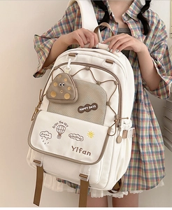 Detail of beige backpack showing multi-compartment design and mushroom pendant accessory