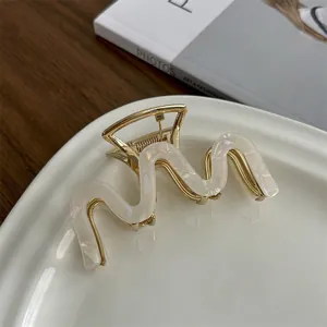 Close-up of pearl white acetate hair claw with gold metal base on a ceramic plate