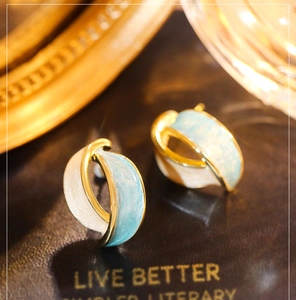 Macro shot of French vintage enamel earrings with gold crossing design and soft blue finish