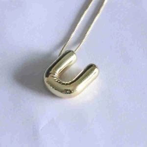 Close-up of a glossy gold bubble letter U pendant necklace with a polished mirror finish