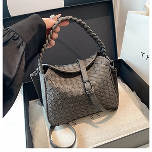 Detailed close-up of a grey woven leather handbag showcased in a black gift box packaging