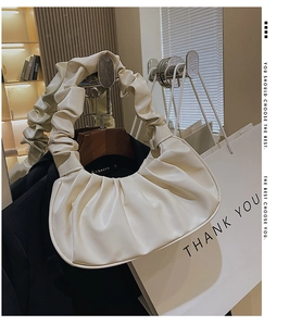 Detail of white pleated cloud handbag with matching handle in a stylish indoor setting