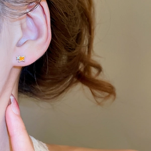 Gros plan d'une boucle d'oreille étoile orange émaillée avec un petit accent de diamant
