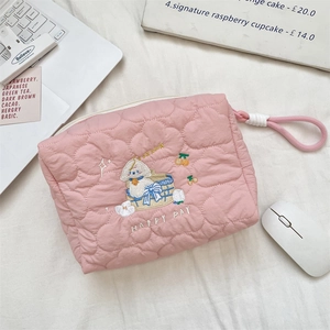 Detailed view of pink quilted makeup bag with puppy embroidery on a desk setup