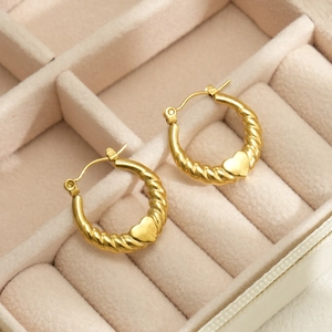Close-up of 18k gold-plated twisted heart hoop earrings in a beige velvet jewelry box