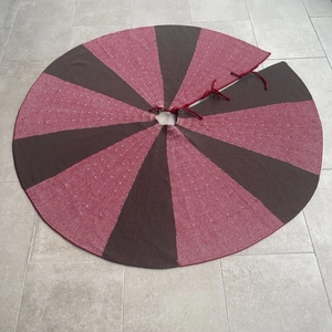 Detail of red and brown knitted Christmas tree skirt with ties on marble floor