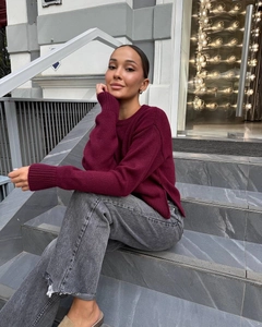 Detail of burgundy knitted sweater with side slit hem paired with grey denim jeans