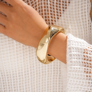 Detailansicht eines breiten, unregelmäßigen goldpolierten Armreifs am Handgelenk für Mode