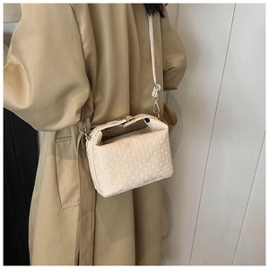 Beige woven crossbody pillow bag with gold hardware worn with a beige trench coat
