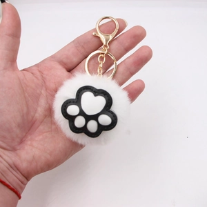 Cute plush cat paw keychain with white pom-pom and gold metal chain held in hand