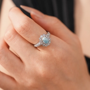 Macro detail of a silver ring featuring a light blue oval stone and zircon halo