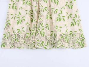 Détail du tissu en dentelle beige avec broderie de feuilles vertes sur l'ourlet