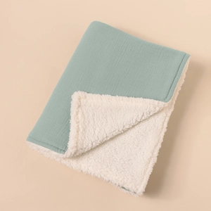 Detail of sage green muslin baby blanket with thick white sherpa lining texture