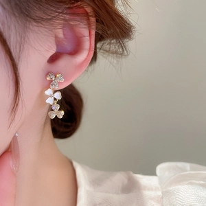 Detail of elegant gold clover drop earrings featuring white mother of pearl and zircons