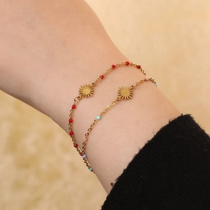 Detail of gold sun pendant bracelets with vibrant red and pastel beads on a model wrist