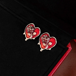Close-up of red enamel heart earrings with gold rose relief in a black velvet jewelry box