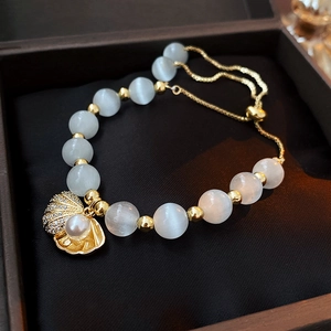 Détail du bracelet ajustable en œil de chat avec coquillage doré et perle dans sa boîte