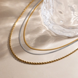 Detail of layered gold rope chain and silver snake chain jewelry set on a beige background