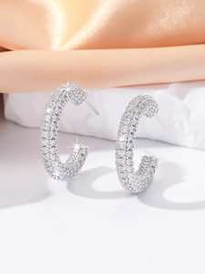 Macro detail of silver C-shaped earrings with pave-set crystals on luxury silk fabric
