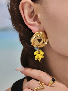 Detail of gold geometric knot earrings with yellow beads and vintage rings on model