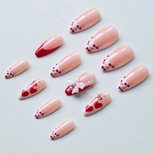 Detail of almond-shaped press-on nails with red cherry designs and 3D pearl bow accents