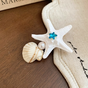 Macro detail of starfish and shell hair clip with pearls and blue star gemstone