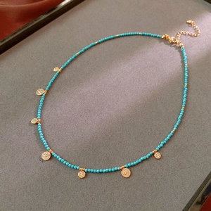 Close-up of blue crystal beaded necklace with golden coin pendants on grey display