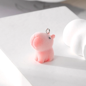 Detail of a pink flocked capybara pendant with silver metal ring on a white platform