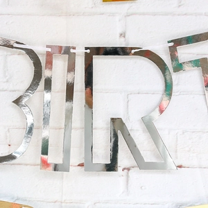 Detail of silver mirror finish Happy Birthday banner letters on white brick wall