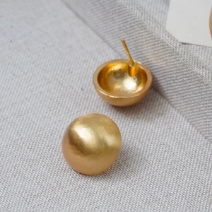 Macro shot of gold hemispherical stud earring with brushed metal texture finish
