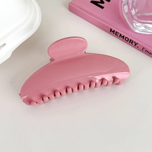 Detail of a large pink acrylic hair claw clip on a minimalist white tabletop setting