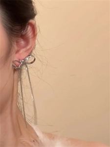 Close-up of silver bow earrings with long chain tassels worn by a model