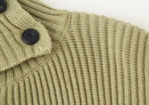 Detailed close-up of rib-knit texture and black buttons on an olive green cardigan