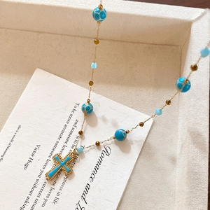 Blue stone beaded necklace with a gold cross pendant on an elegant jewelry box background
