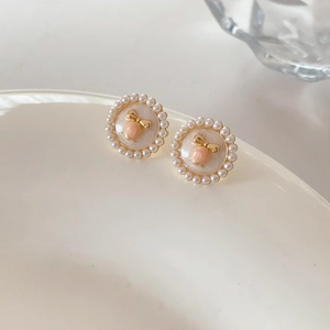 Detail of round pearl stud earrings with pink peach motif and golden bow accent