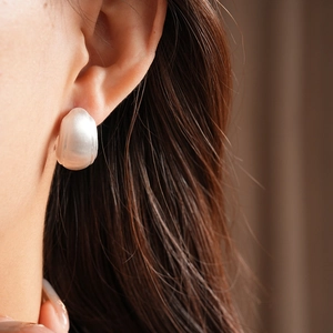 Close-up of matte silver square geometric earrings worn on a model earlobe