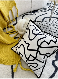 Detailed view of velvet pillow featuring black abstract lines on a textured white carpet