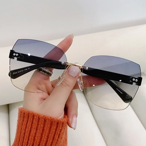 Fashionable rimless oversized gradient sunglasses with gold metal accents held by hand