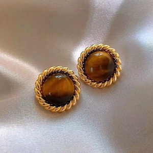 Close-up of vintage gold twist earrings with brown tiger eye stone on silk fabric