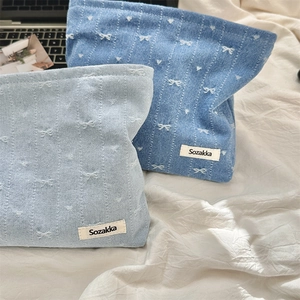 Detail of denim cosmetic bags with white bow embroidery on textured white fabric