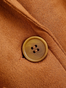 Dettaglio macro del bottone ambra e della texture in camoscio sul blazer caramello
